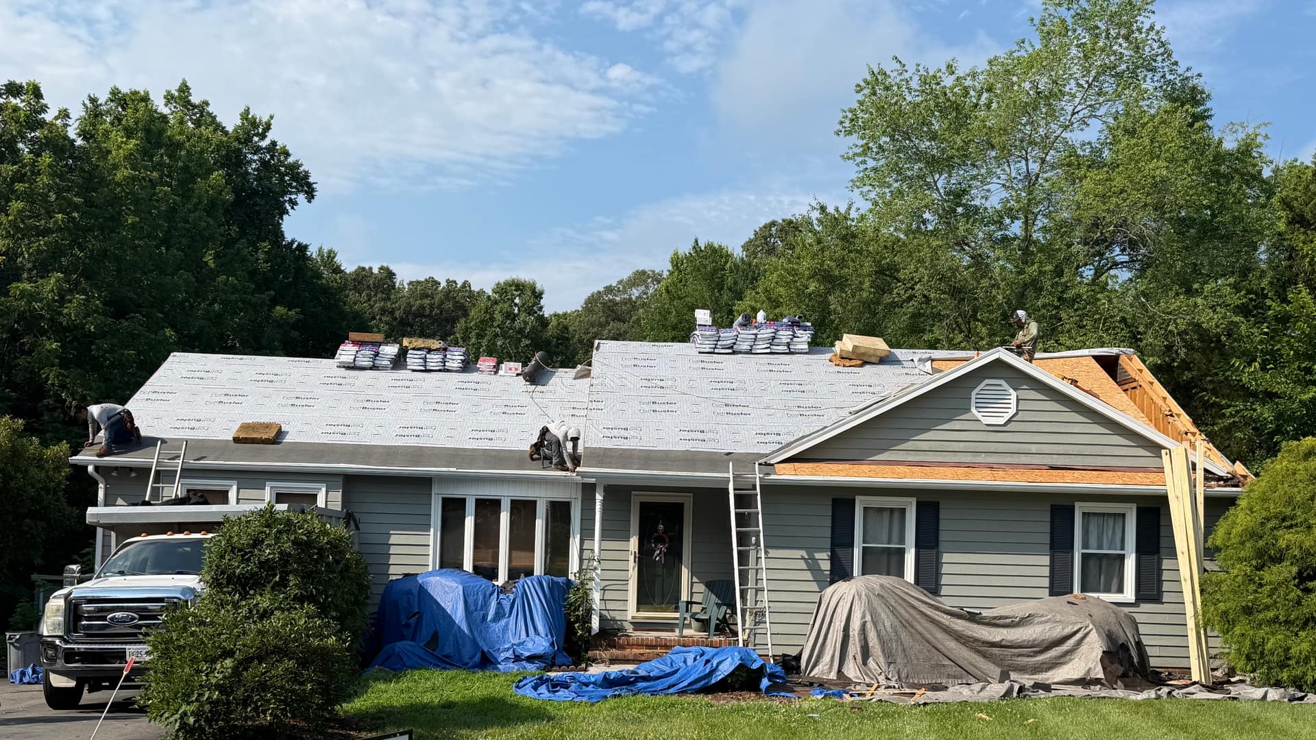 DHBerry Construction crew installing a new roof, with the company sign in the front yard
