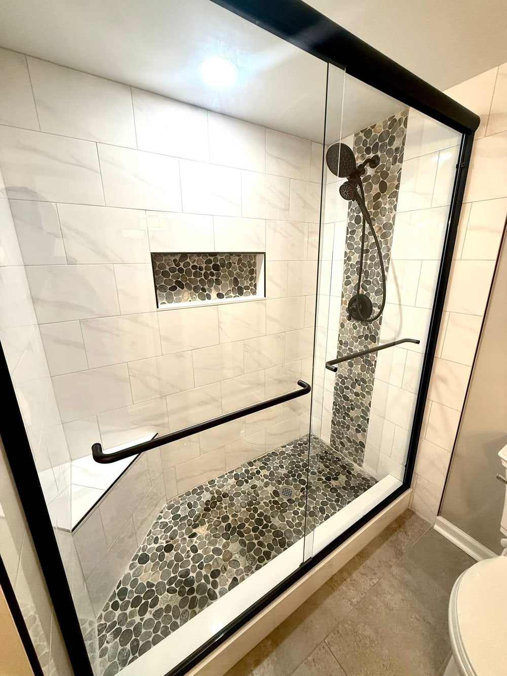 Walk-in shower with marble-look tile and pebble mosaic floor